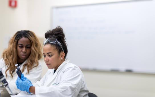 Two women carefully inspecting a handheld instrument in a lab