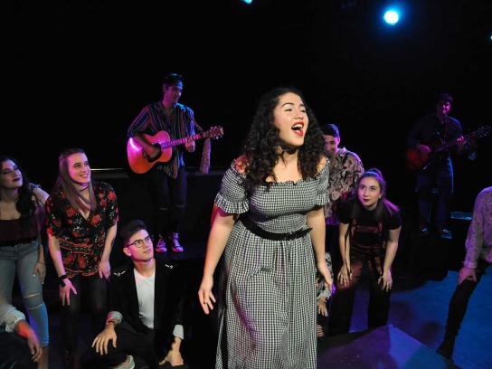 CCPA music student singing on stage in a black-and-white checked dress