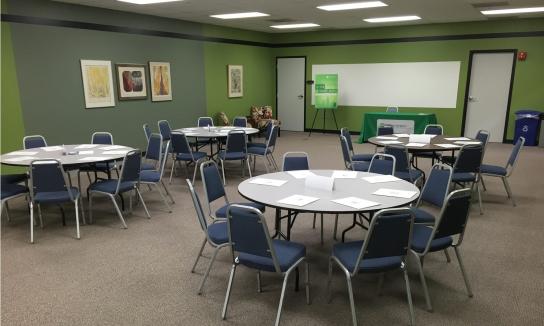 A mid-sized carpeted room with white boards and with tables and chairs.