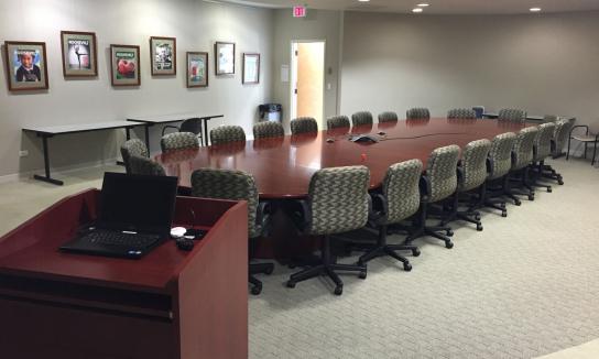Large oblong board room table with chairs and a podium.