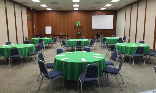 Large room with wood panelled walls featuring numerous round tables and chairs.